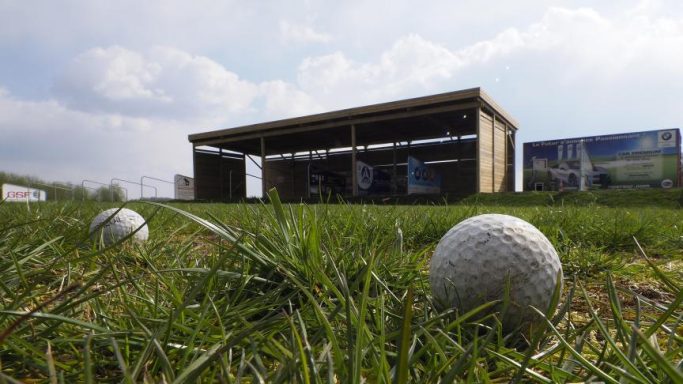 Un terrain de golf avec des balles sur l'herbe et un abri en arrière-plan.